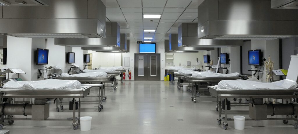 Anatomie-Schulungslabor mit Tischen beidseitig eines Mittelgangs und Monitoren, verbunden mit dem Alphadidact Schulungssystem.