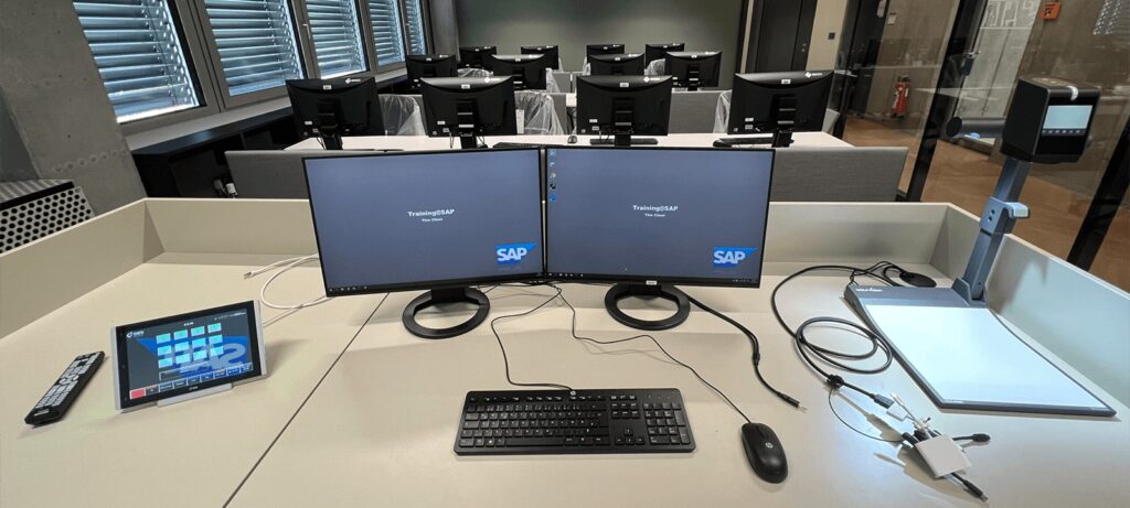 Dozentenpult mit Dual-Monitor-Setup und Alphadidact Touchscreen im SAP-Raum, gesteuert durch das Alphadidact-System.